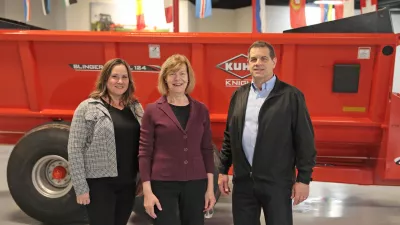 U.S. Senator Tammy Baldwin, Kuhn North America President Greg Petras and AEM President Megan Tanel stand for a photo in front of a piece of KUHN equipment. 