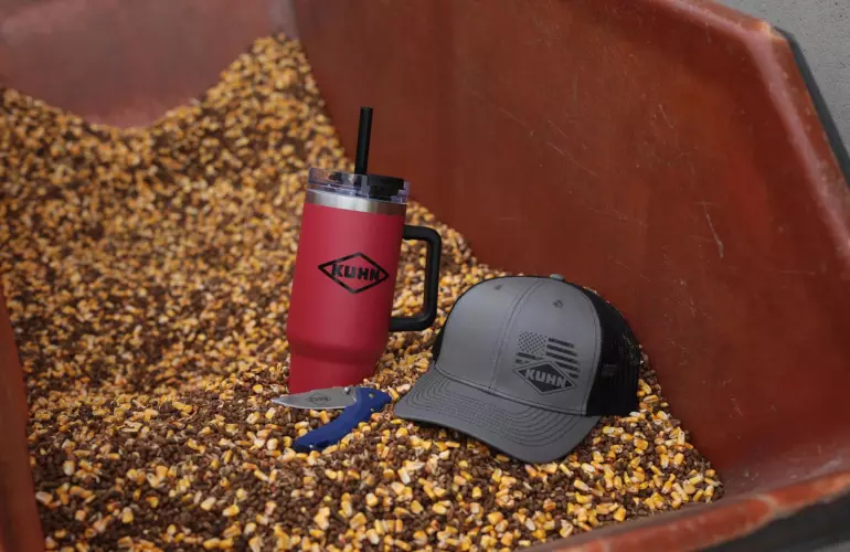 KUHN tumbler, pocket knife and cap in a bin of feed