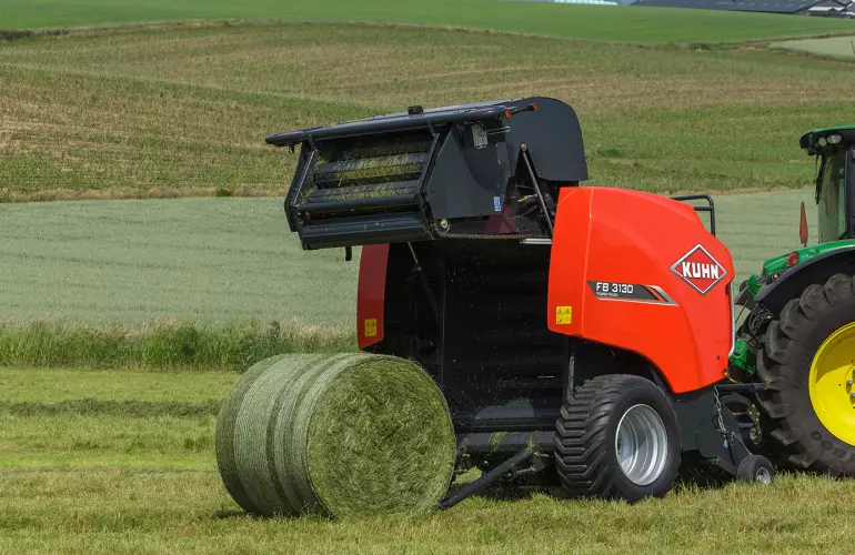 KUHN FB 3130 round baler producing a net bound grass bale in a hilly area.
