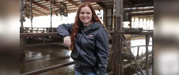 Woman stands in dairy barn wearing a grey KUHN jacket