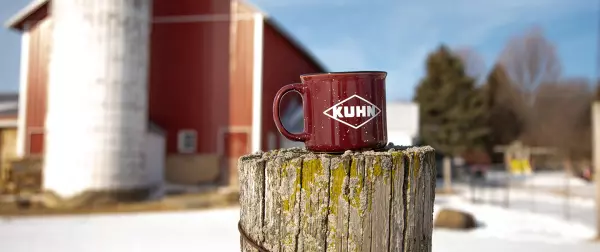 KUHN coffee mug sits on a post in front of a red barn