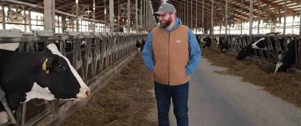 Man stands in dairy barn with KUHN hat and vest