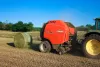 A VB 3165 Round baler ejecting a bale in the distance